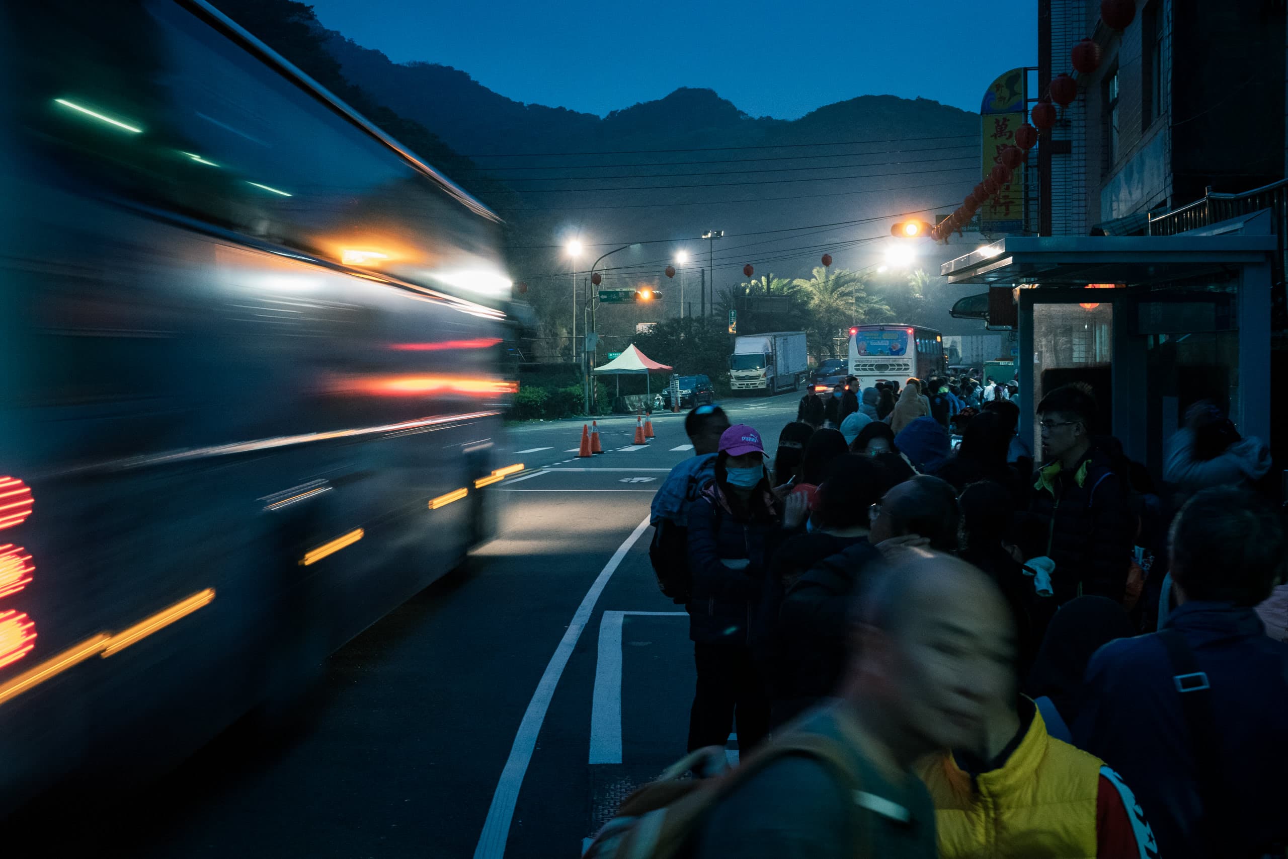 Crowd lining up by the street with a bus passing by on the left