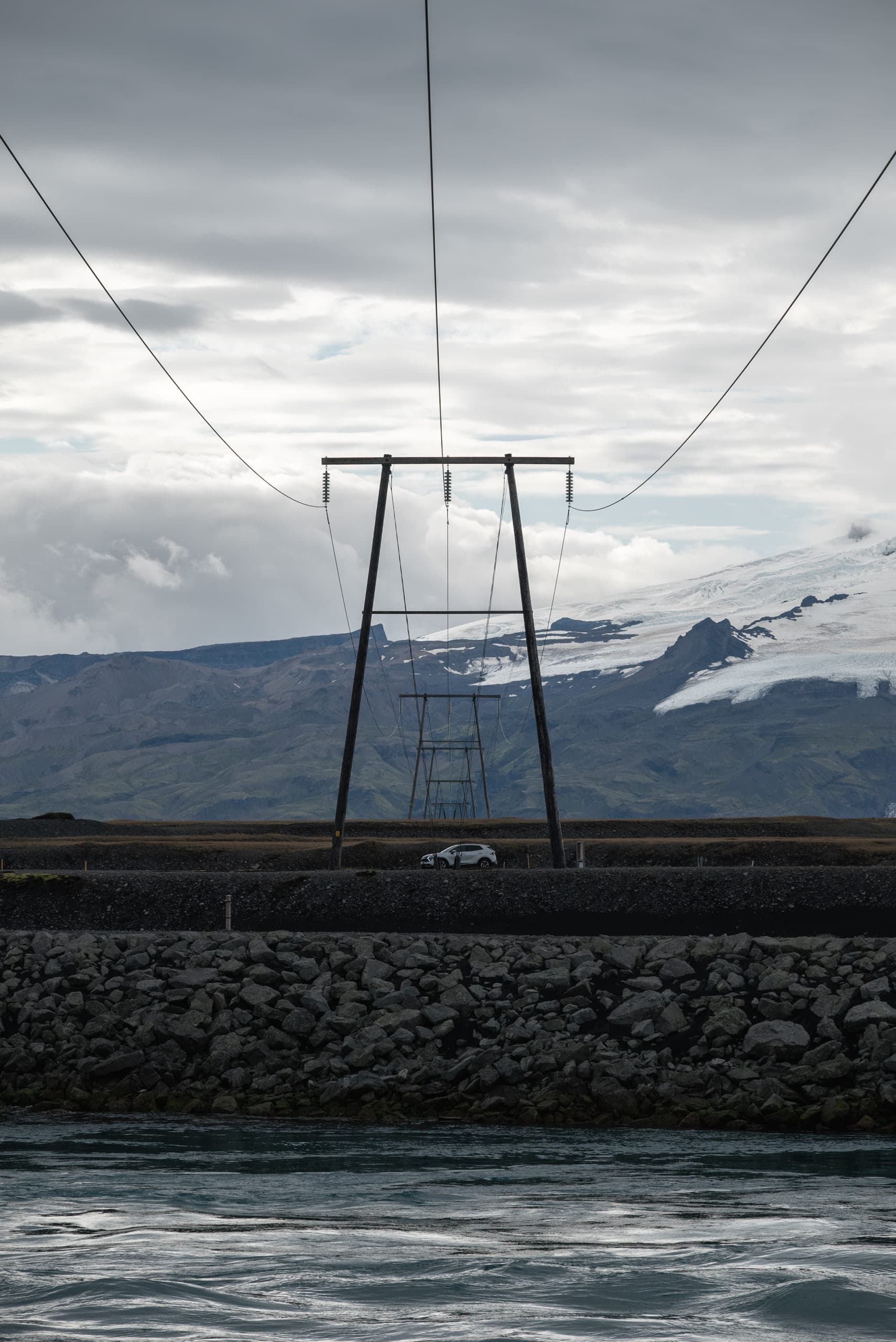 A car in the center driving across a road and power lines cascade into the distance at the center