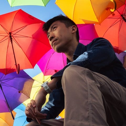 Charlie Chao looking up while sitting under colorful umbrellas