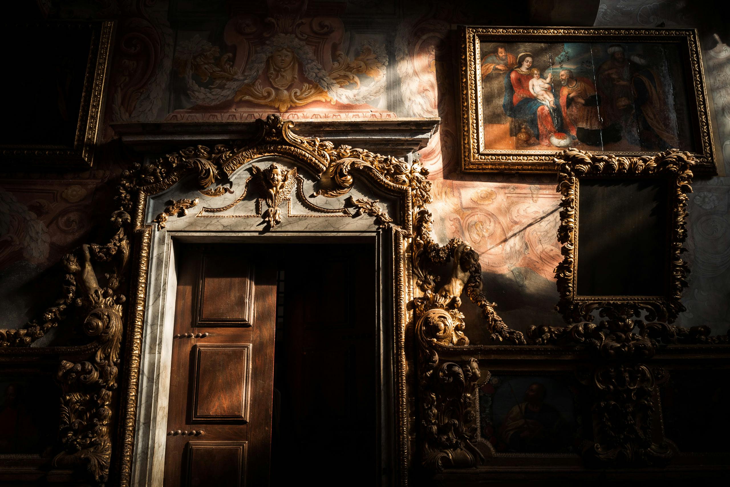 Gallery wall with ornate paintings on the wall, a large door, and a dramatic lighting