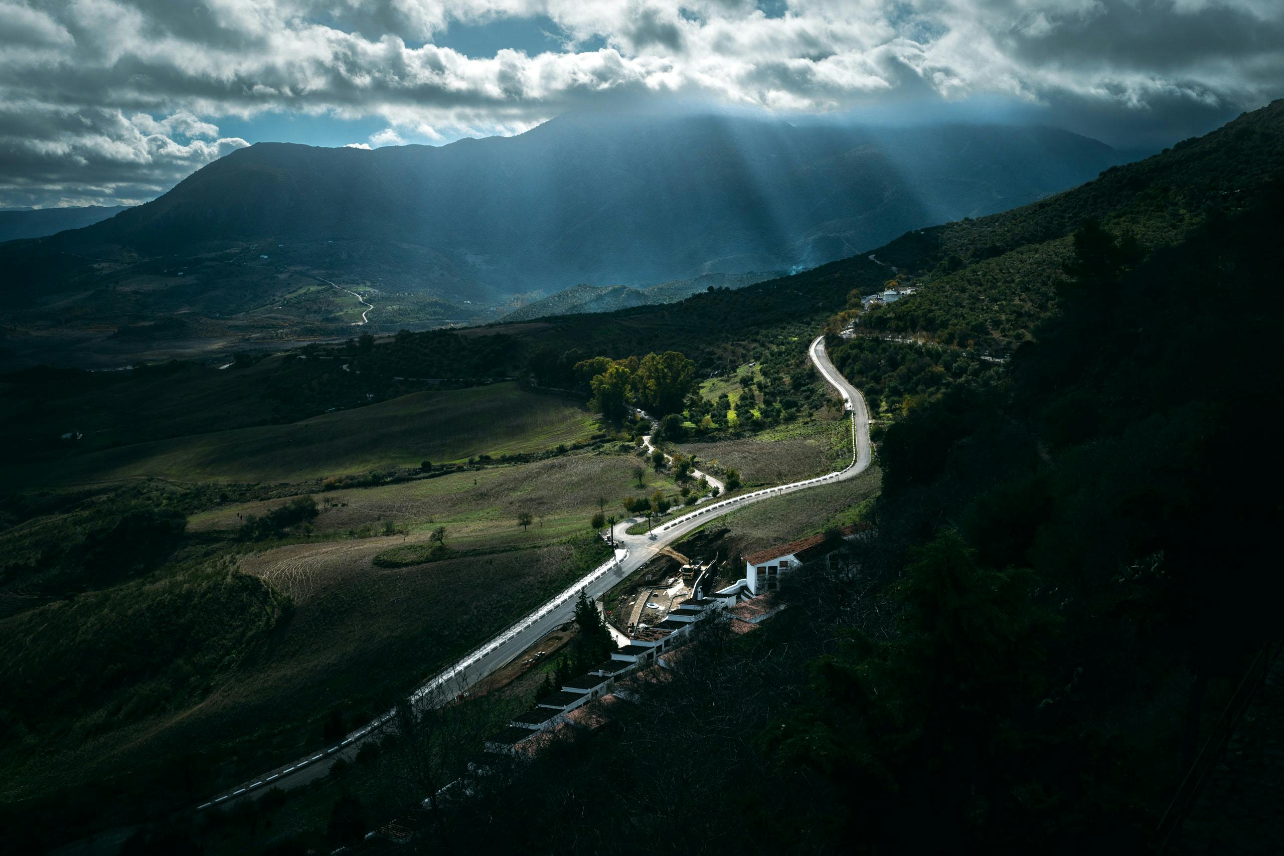 View of a road illuminated by streams of light from the cloudy sky